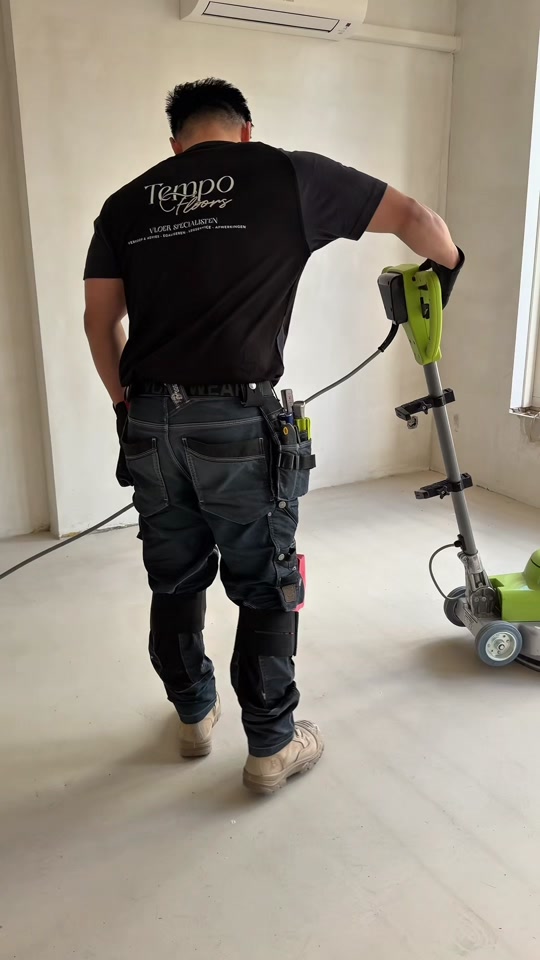 Een vloerenlegger in een TempoFloors-shirt slijpt een geëgaliseerde vloer